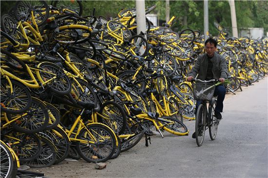 중국 베이징에 거주하는 한 중국인이 공유 자전거 회사 오포의 수리 센터에 수북이 쌓인 고장 난 자전거 옆을 지나고 있다. (사진=EPA연합)
